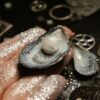 From above of female hand showing sparkling pearl in mollusc seashell on hand on blurred background